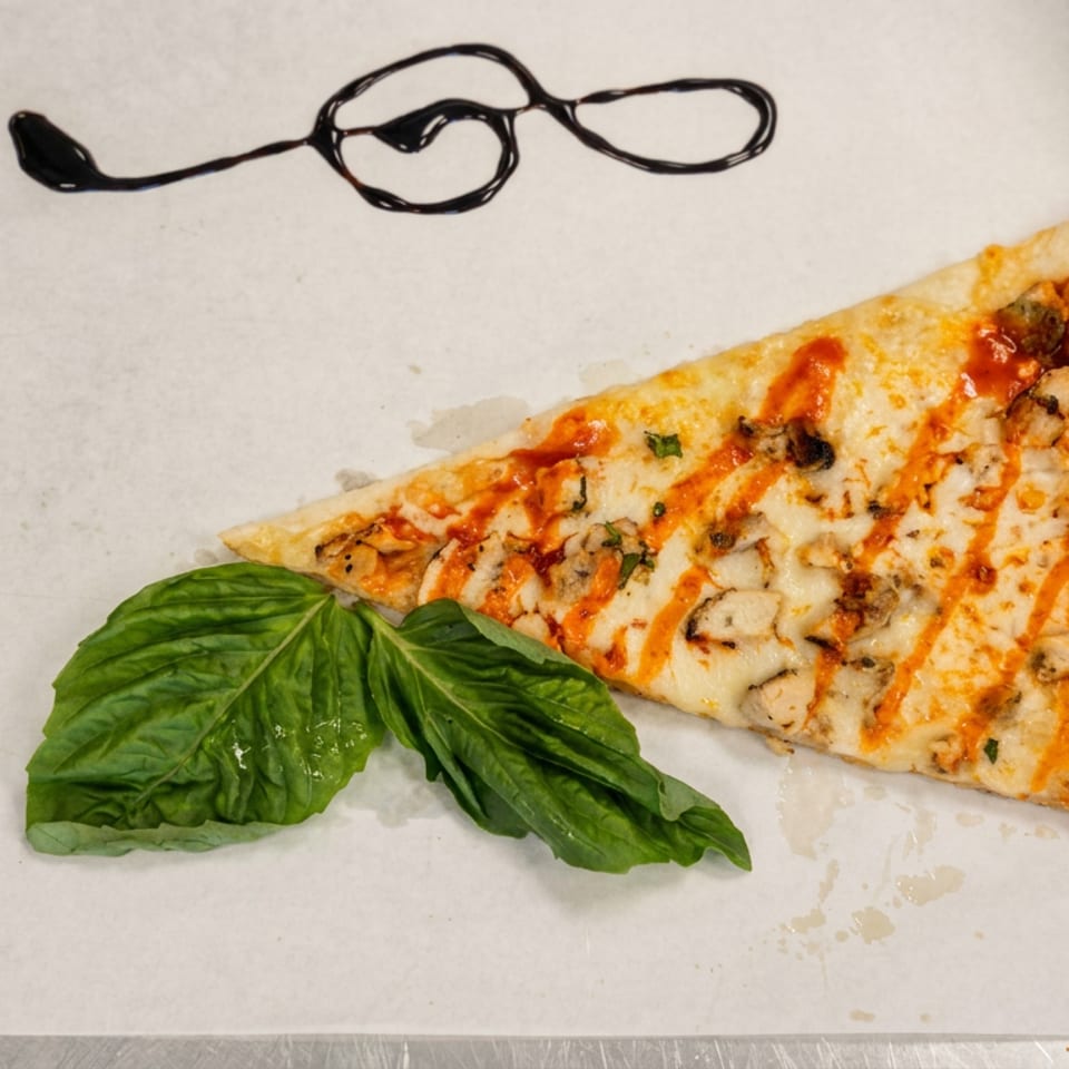 Rectangular slice of cheesy pizza drizzled with tomato sauce, garnished with fresh basil on a metal serving tray.